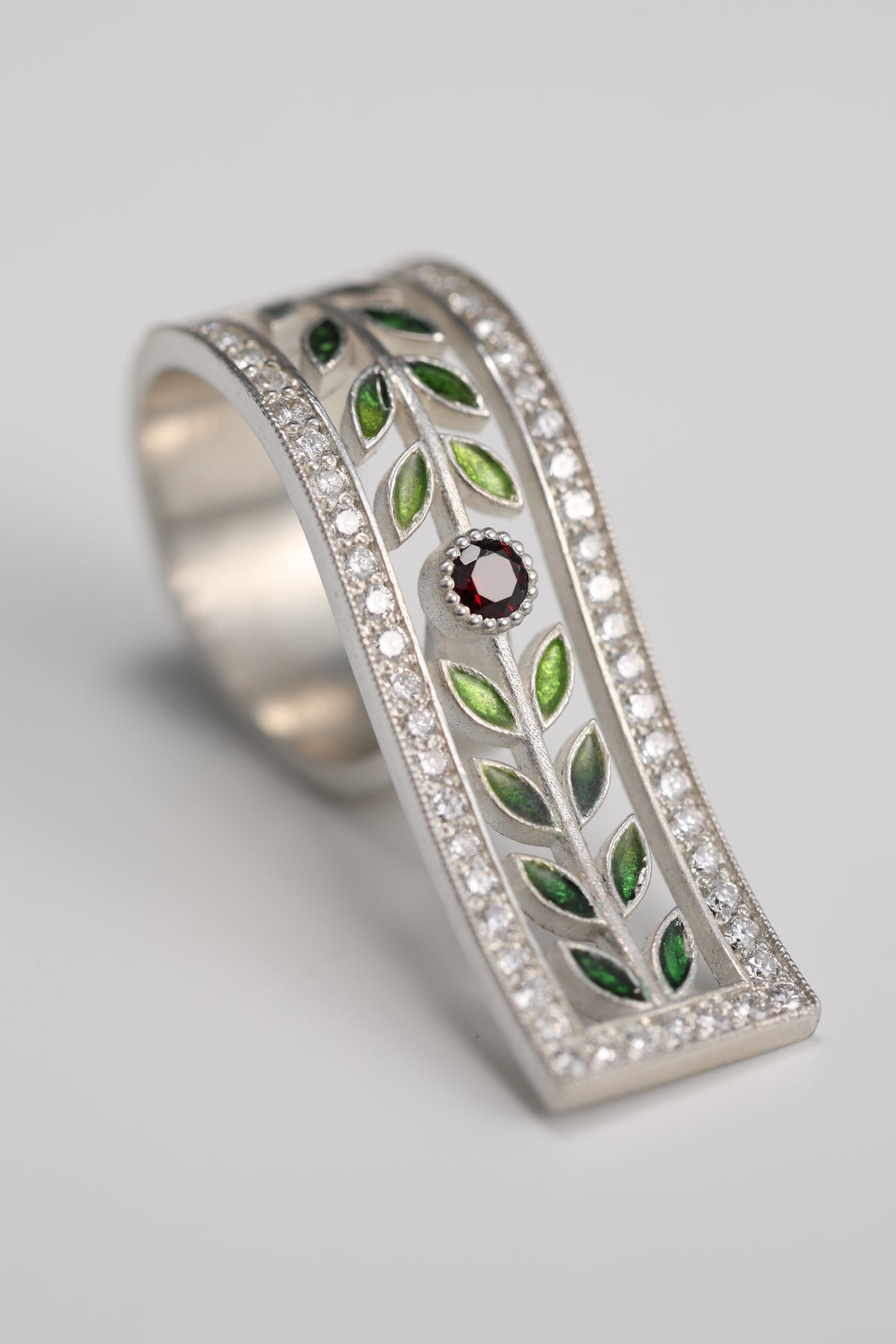 Silver jewelry with green enamel leaves and a red gemstone