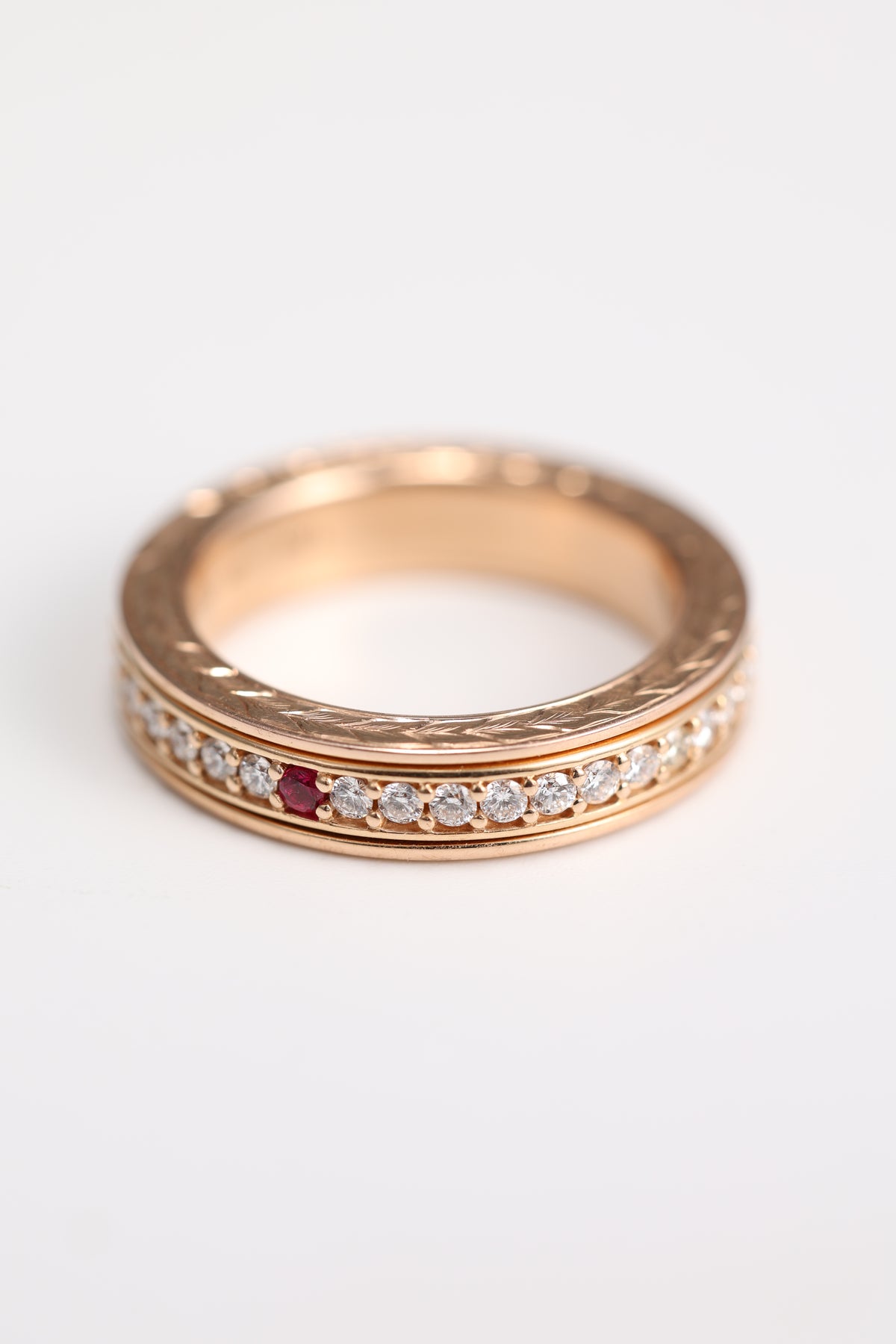 Handmade 18K rose gold spinner ring with natural ruby, diamonds, and hand-engraved sides, angled front view